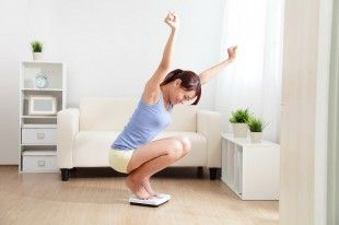 26160063 – happy woman smiling on weighing scales at home, asian