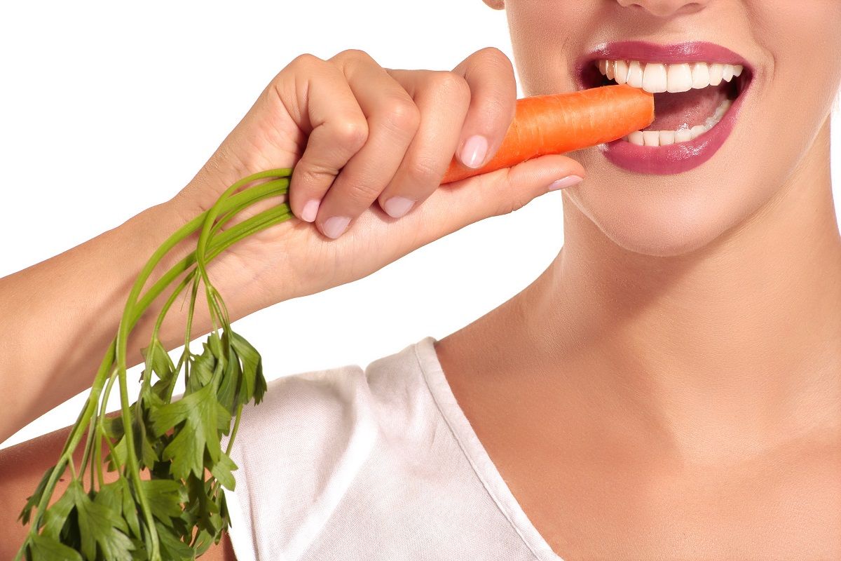The beautiful girl in a white shirt bites carrots