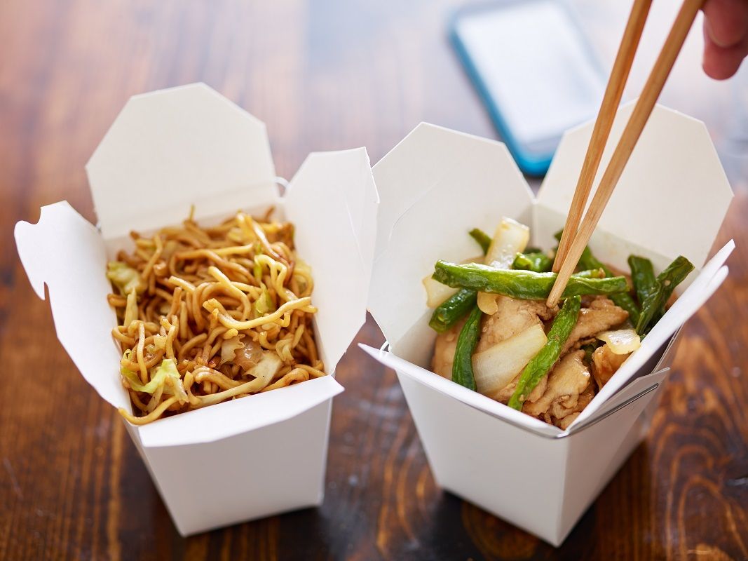 eating chicken and greenbeans out of chinese take out box with chopsticks