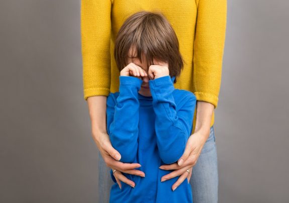 Sad little child, boy, hugging his mother at home, isolated imag
