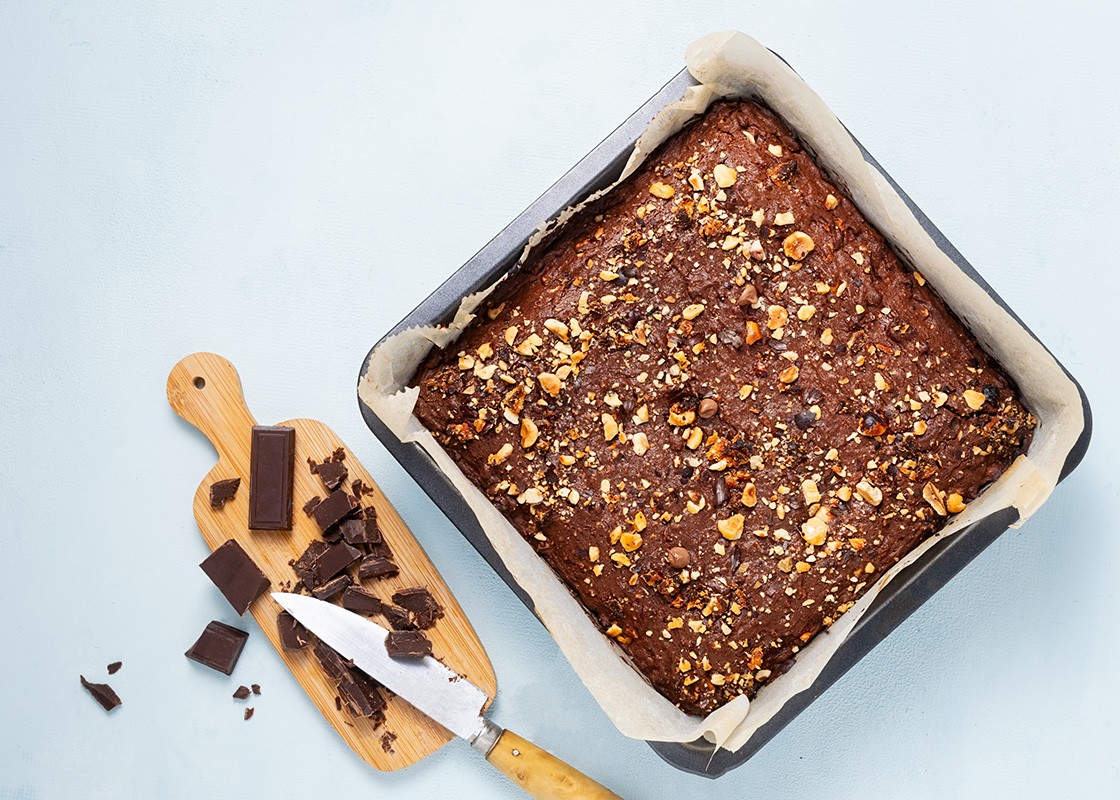 Chocolate brownie cake, dessert with nuts and fruits on dark background, directly above. Diet concept, vegan.