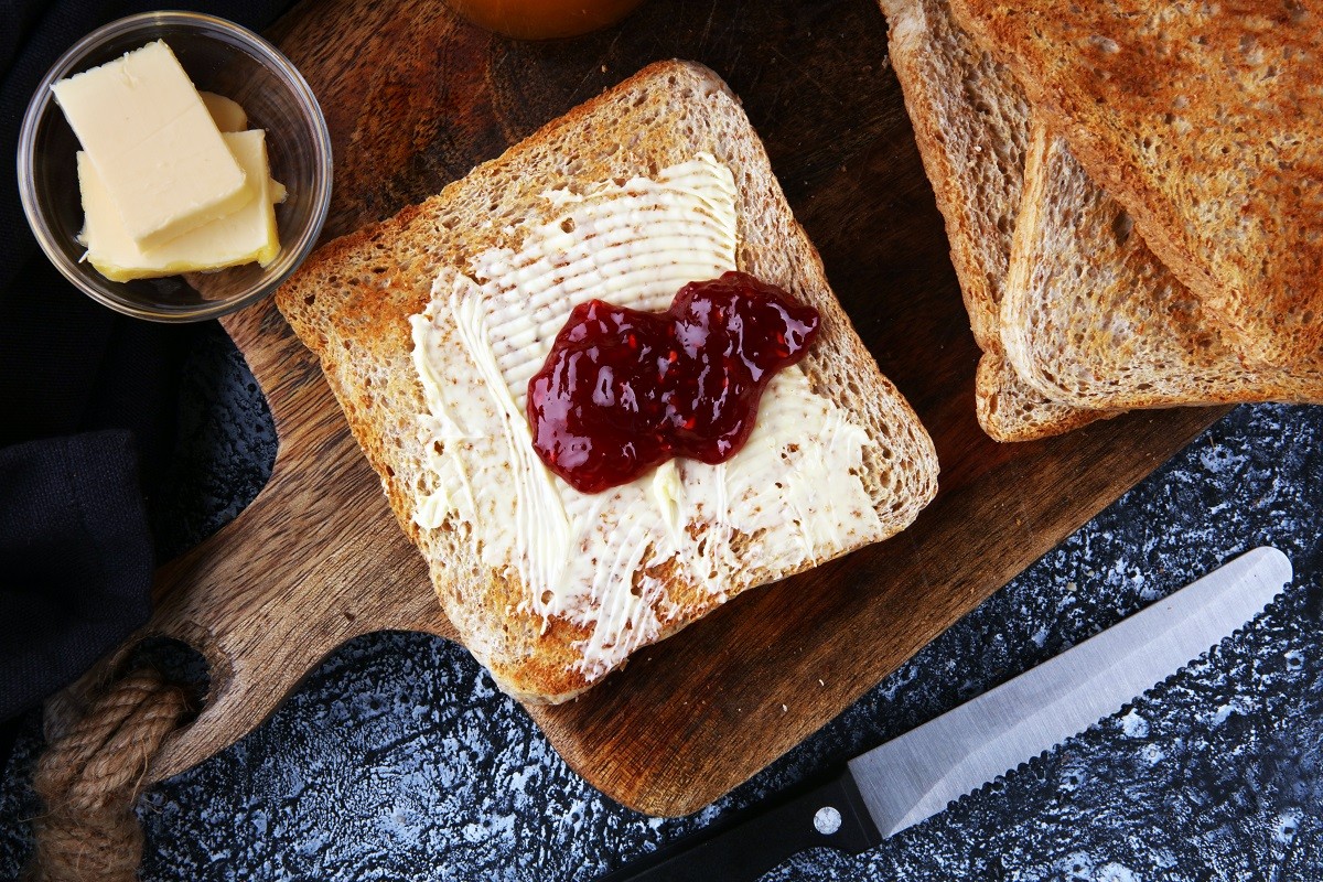 Toast bread with homemade strawberry jam and orange marmalade on rustic table served with butter for breakfast or brunch.