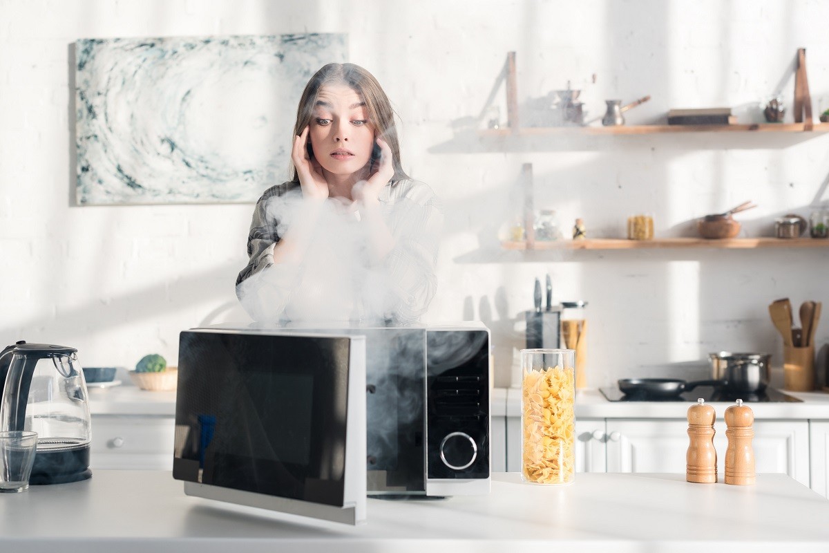 shocked and attractive woman looking at broken microwave in kitchen