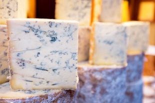 Stacks of whole and cut Stilton cheeses for sale at a market