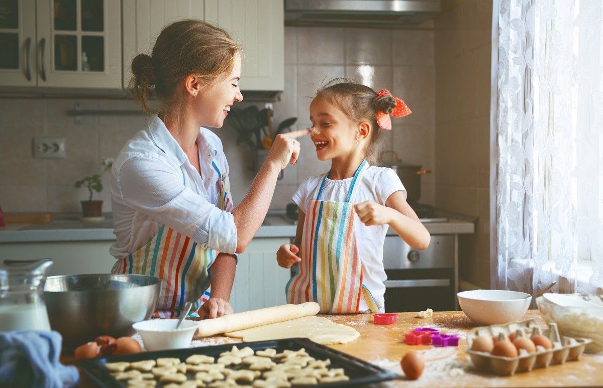 Happy family mother and daughter bake kneading dough in kitchen