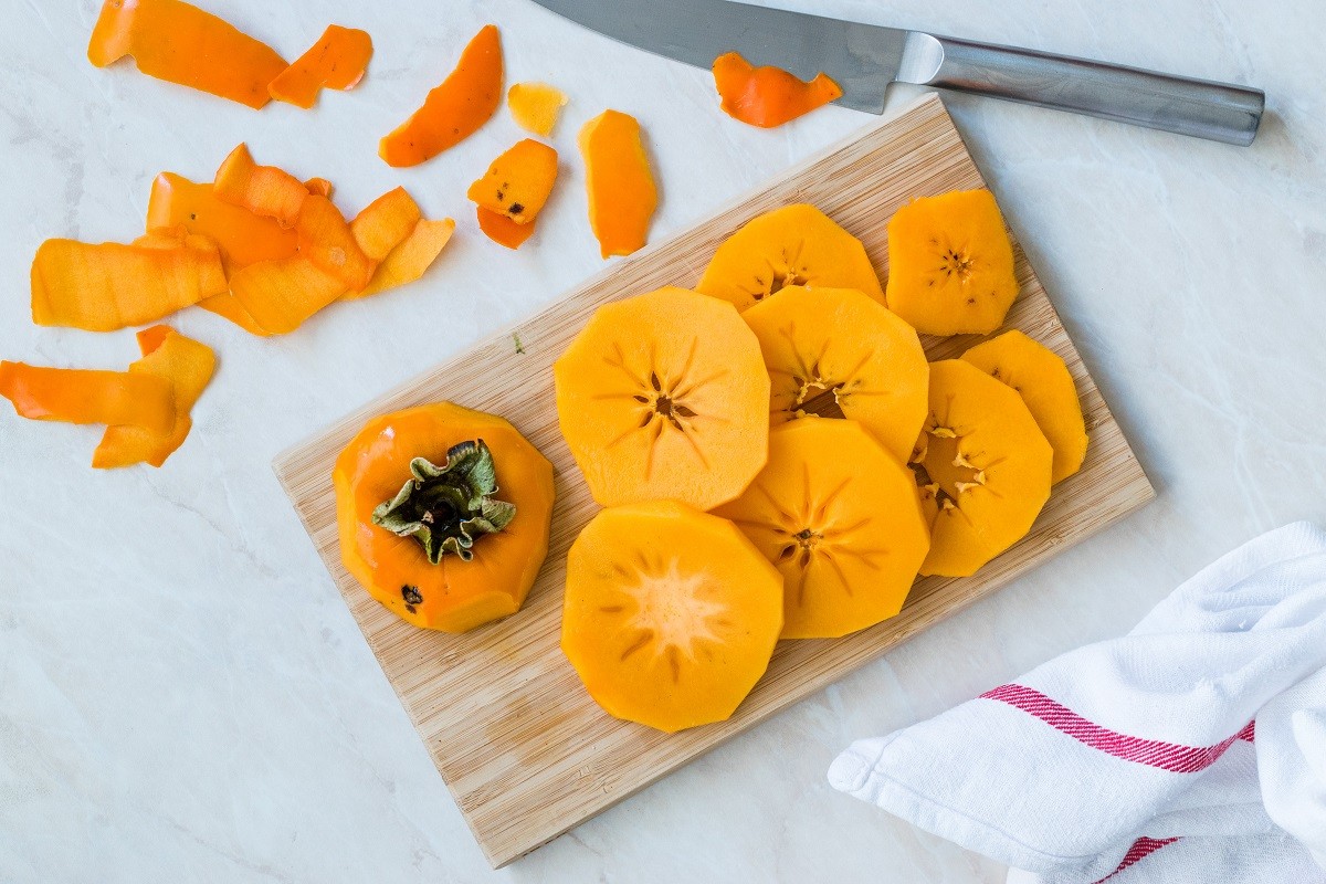 Sliced Persimmon Fruit Slices on Wooden Board with Knife.
