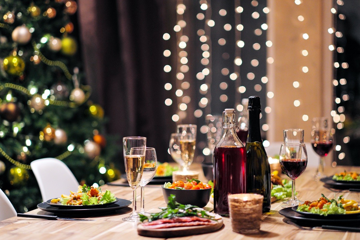Festive table setting. Food and drinks, plates and glasses. Evening lights and candles. New Year’s Eve.