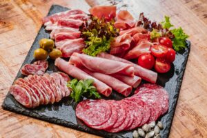 Different types of sausages with sauce served on wooden table.Cold cuts of different types of sausages on a black flat plate on a wooden table with vegetables. Super food.