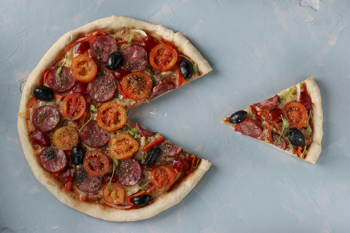 Pizza with a cut out piece on a light blue background, Closeup