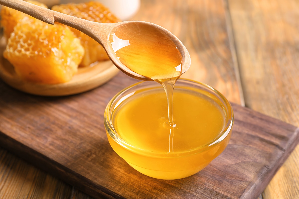 Honey,Pouring,From,Spoon,Into,Glass,Bowl,On,Table,,Closeup