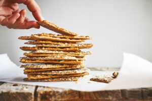 Womans,Hand,Takes,Crunchy,Crispbread,On,Recycled,Paper,On,Wooden