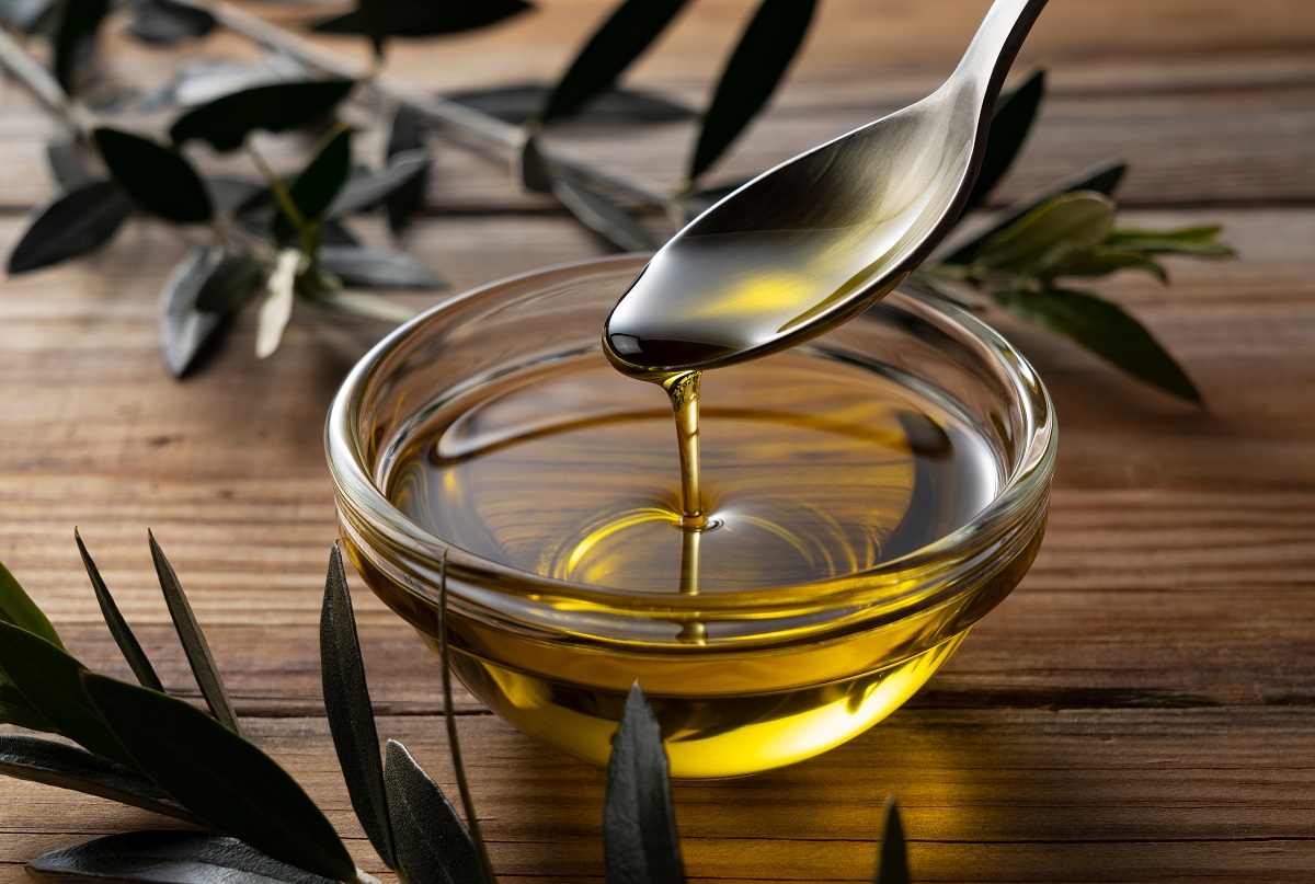 Spooning,Olive,Oil,Into,A,Bowl,Placed,On,A,Wooden