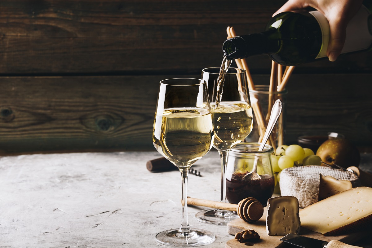 White,Wine,Pouring,Into,Glasses,With,Charcuterie,Assortment,On,T