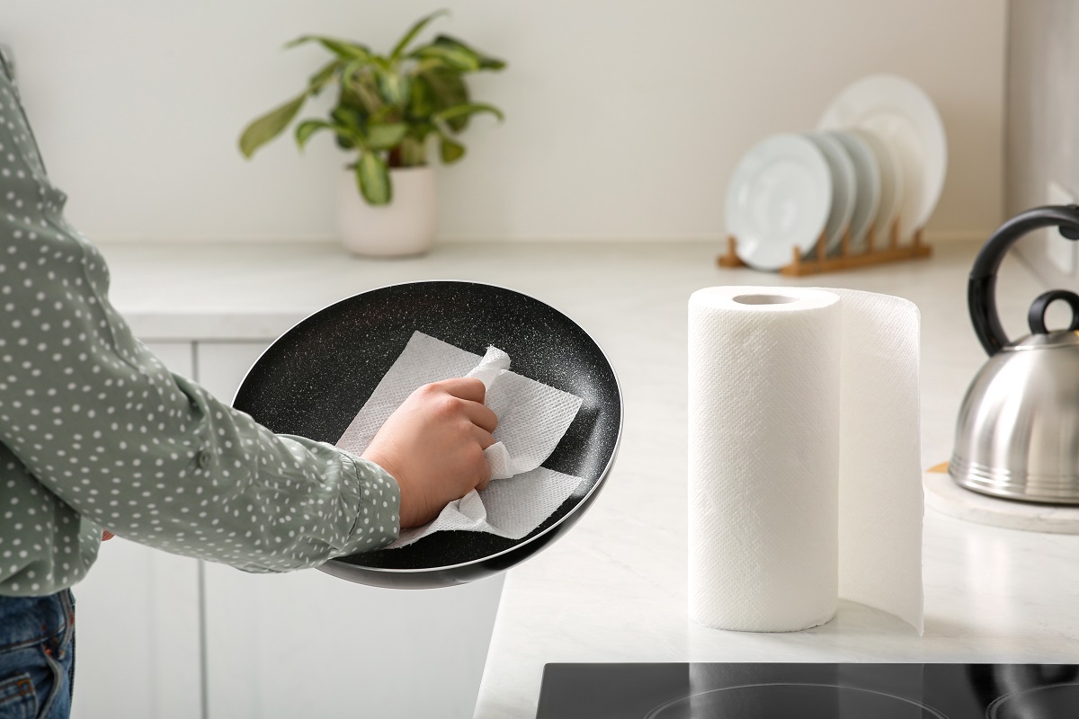 Woman,Wiping,Frying,Pan,With,Paper,Towel,In,Kitchen,,Closeup
