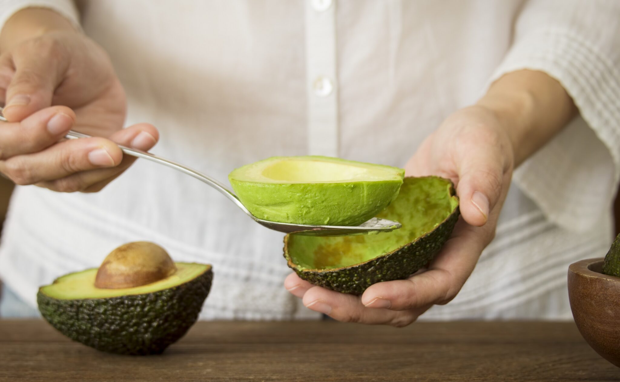 Woman,Use,A,Spoon,To,Scoop,The,Avocado,Out,Of
